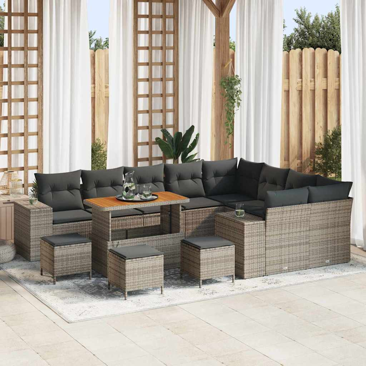 Ein Outdoor-Wohnset mit Ecksofa, Couchtisch, Ottomanen und Vorhängen. Das Set steht auf einem Teppich in einer Terrasse.