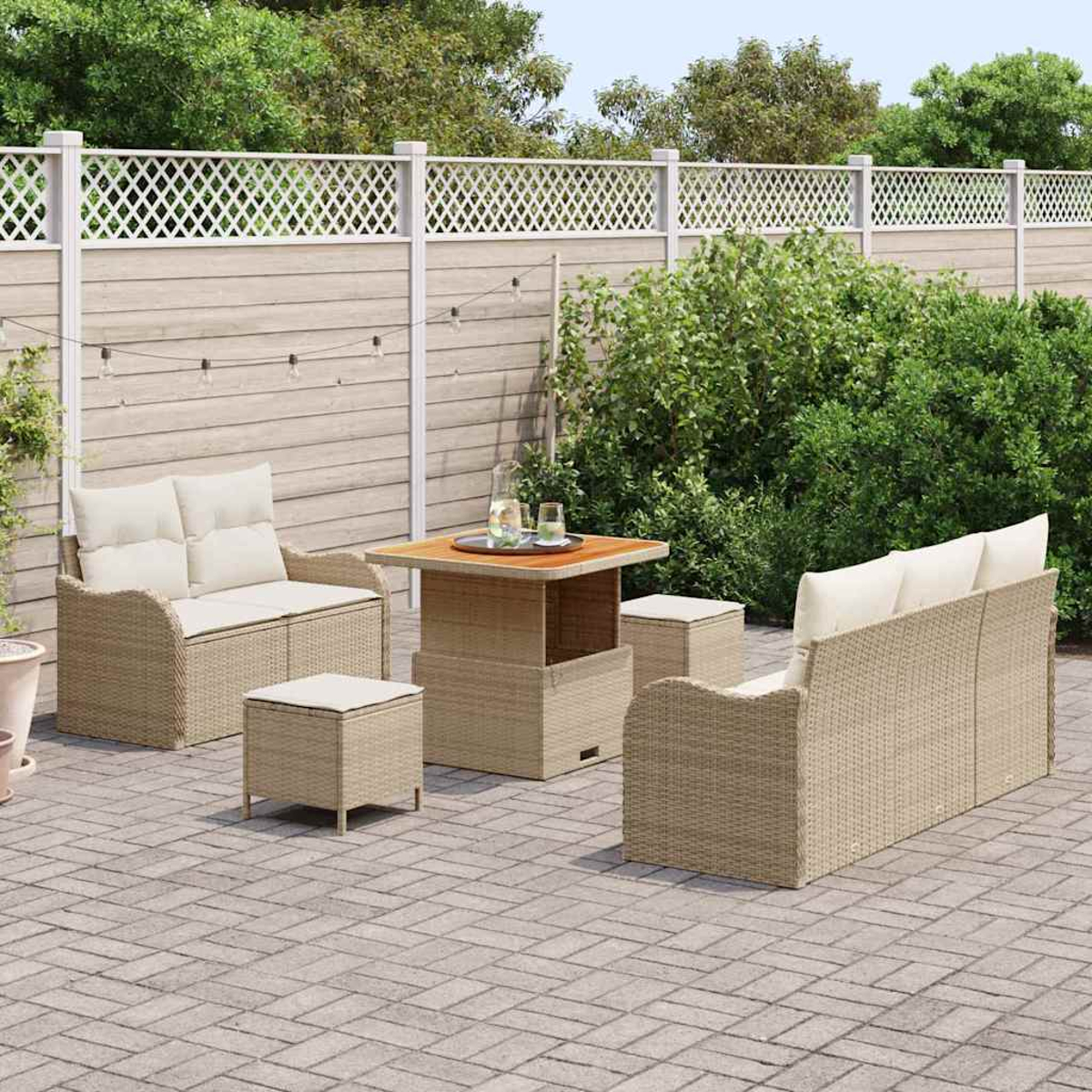 Garten-Set mit beigefarbenen Möbeln, Couchtisch und Kissen. Grüne Büsche und weißer Zaun im Hintergrund.