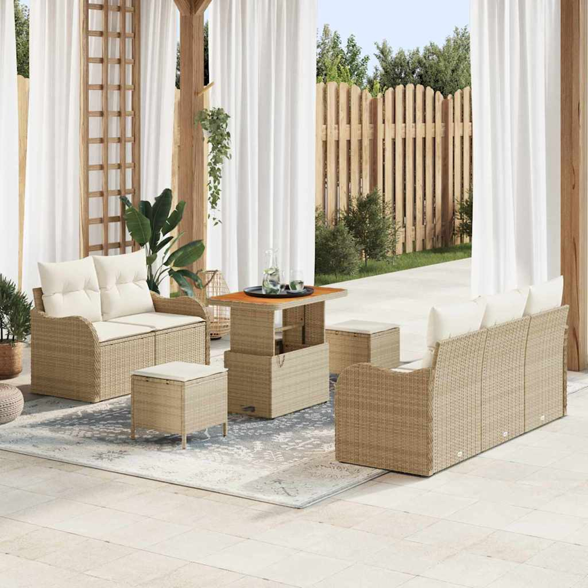 Terrassenmöbel-Set mit Korbmöbeln, weißen Kissen und einem Holztisch. Transparente weiße Vorhänge und ein Holzzaun im Hintergrund.