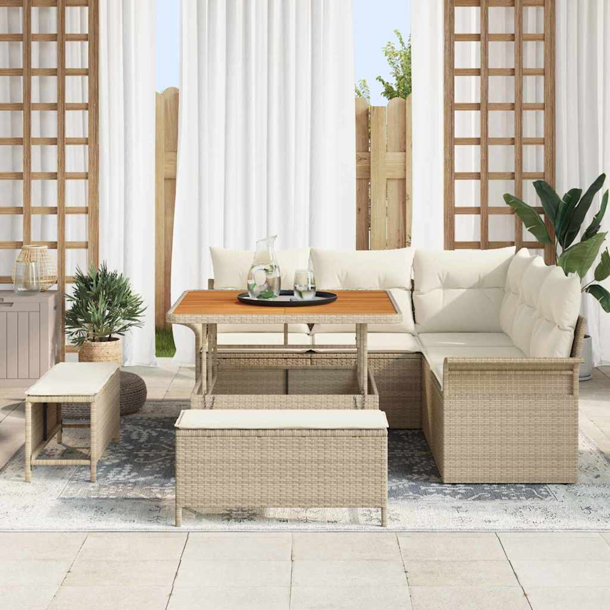 Outdoor-Sitzbereich mit beigen Korbmöbeln, einem Holztisch und weißen Kissen. Transparente Vorhänge und Pflanzen sind sichtbar.