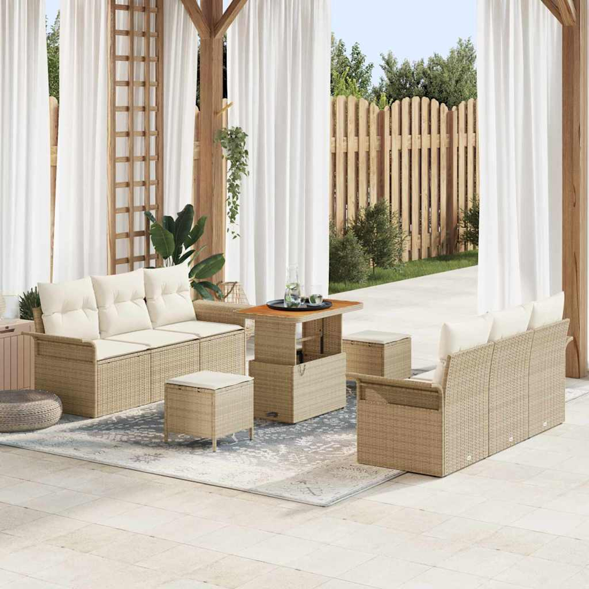 Set da patio con divani in vimini, tavolo e pouf. Tende bianche e recinzione in legno sullo sfondo. Cuscini beige.