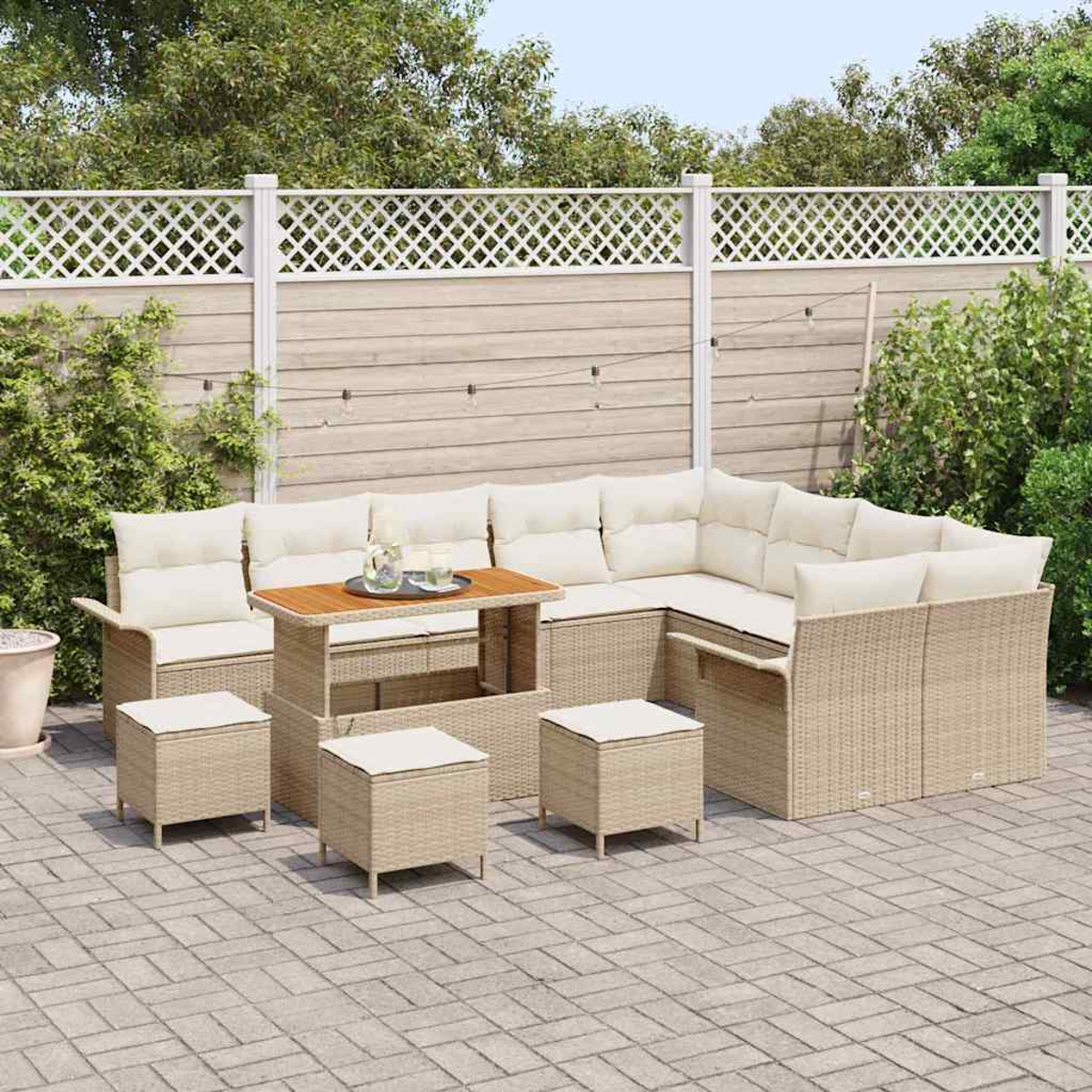 Gartenmöbel-Set aus Korbgeflecht auf einer Terrasse. Enthält ein Ecksofa, einen Tisch und Hocker, alle mit cremefarbenen Kissen.