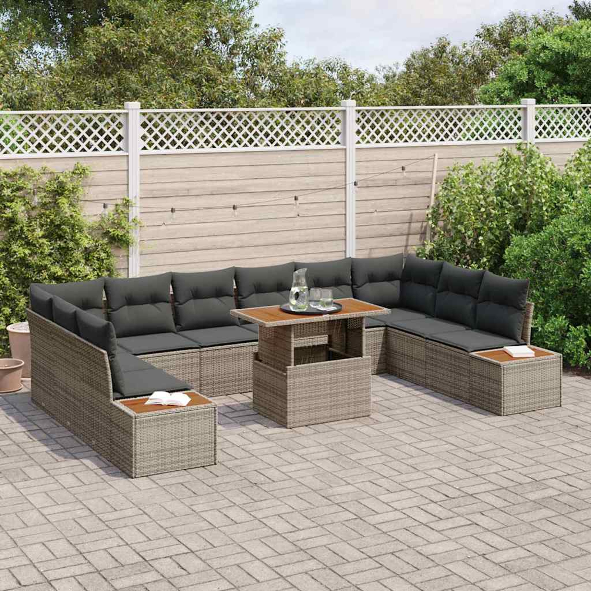 Sofá seccional para exteriores con cojines grises y una mesa de madera. En un patio con valla blanca y follaje verde al fondo.