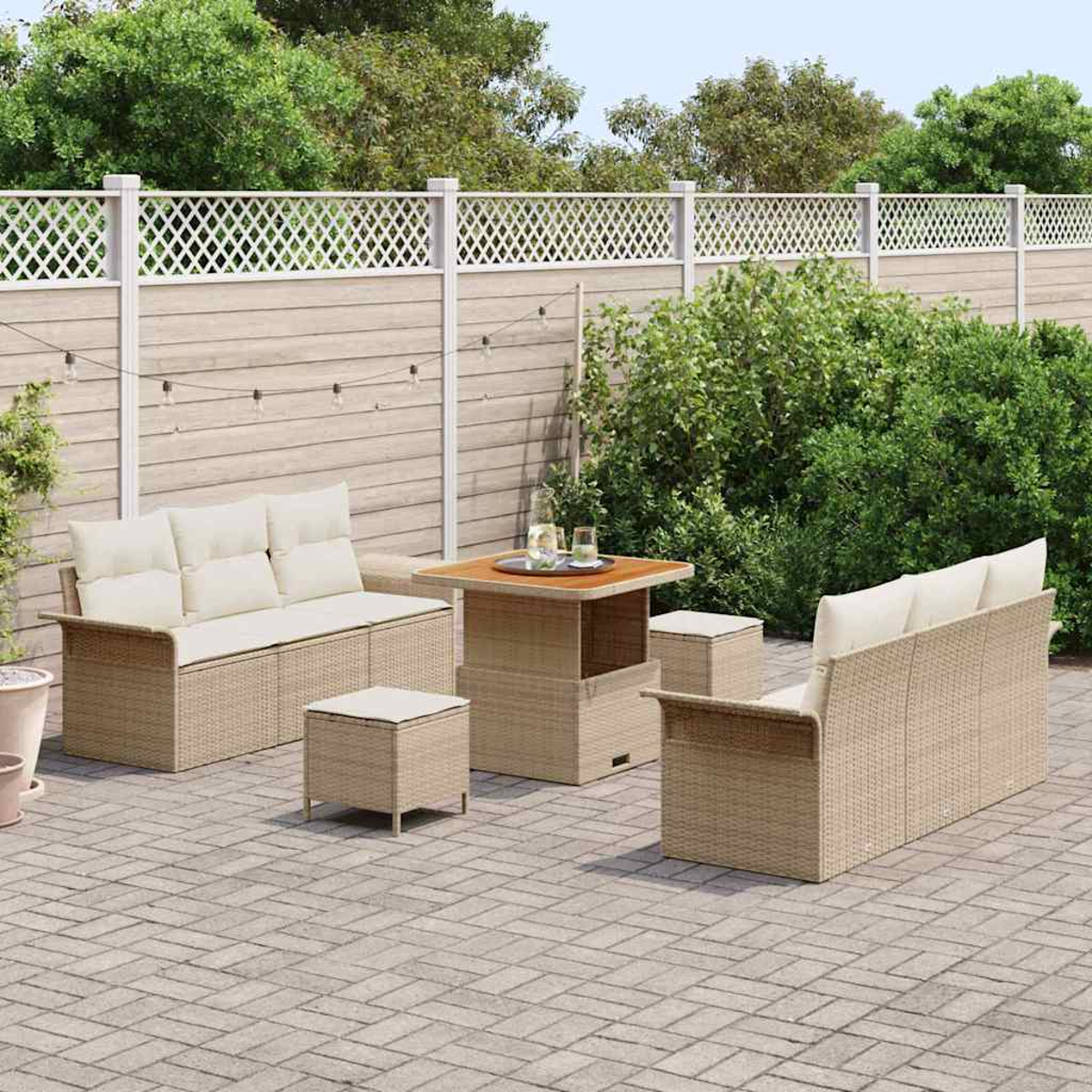 Garten-Set: zwei Sofas, zwei Hocker und ein Tisch auf einer Ziegelterrasse. Ein weißer Zaun und Grün im Hintergrund.