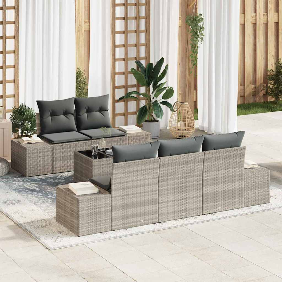 Gartenmöbel mit grauen Kissen, einem kleinen Glastisch und Pflanzen. Hintergrund: weiße Vorhänge und Holzstrukturen.