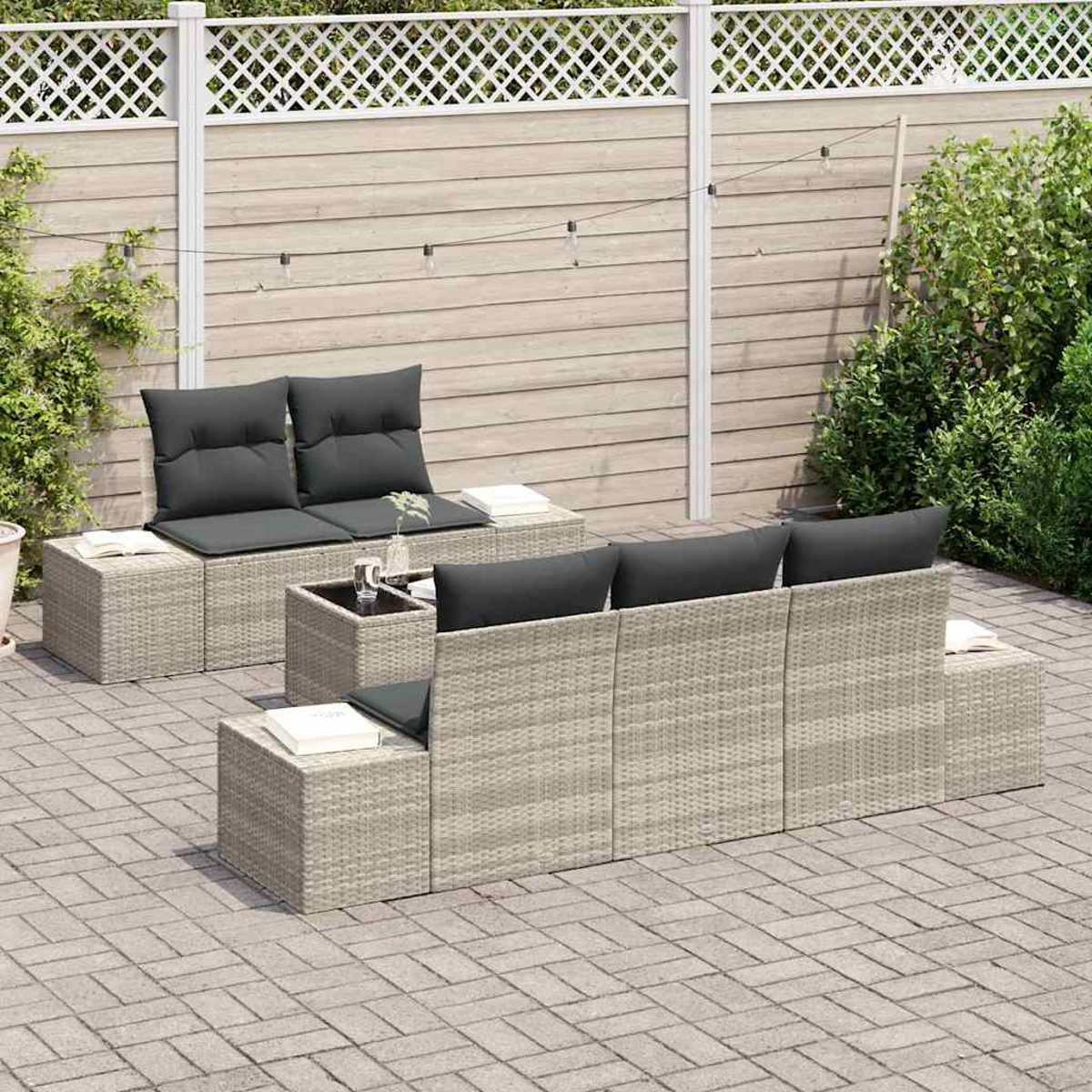 Terrassenset mit grauen Kissen. Enthält ein Sofa, zwei Stühle und einen kleinen Tisch. Holzzaun und Grün im Hintergrund.