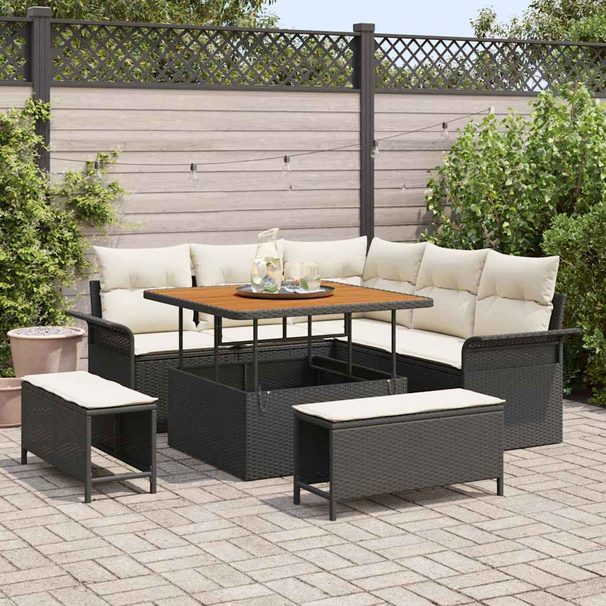 Terrassenmöbel-Set mit Tisch, Bänken und Ecksofa. Das Set steht auf einer Backstein-Terrasse mit Holzzaun im Hintergrund.