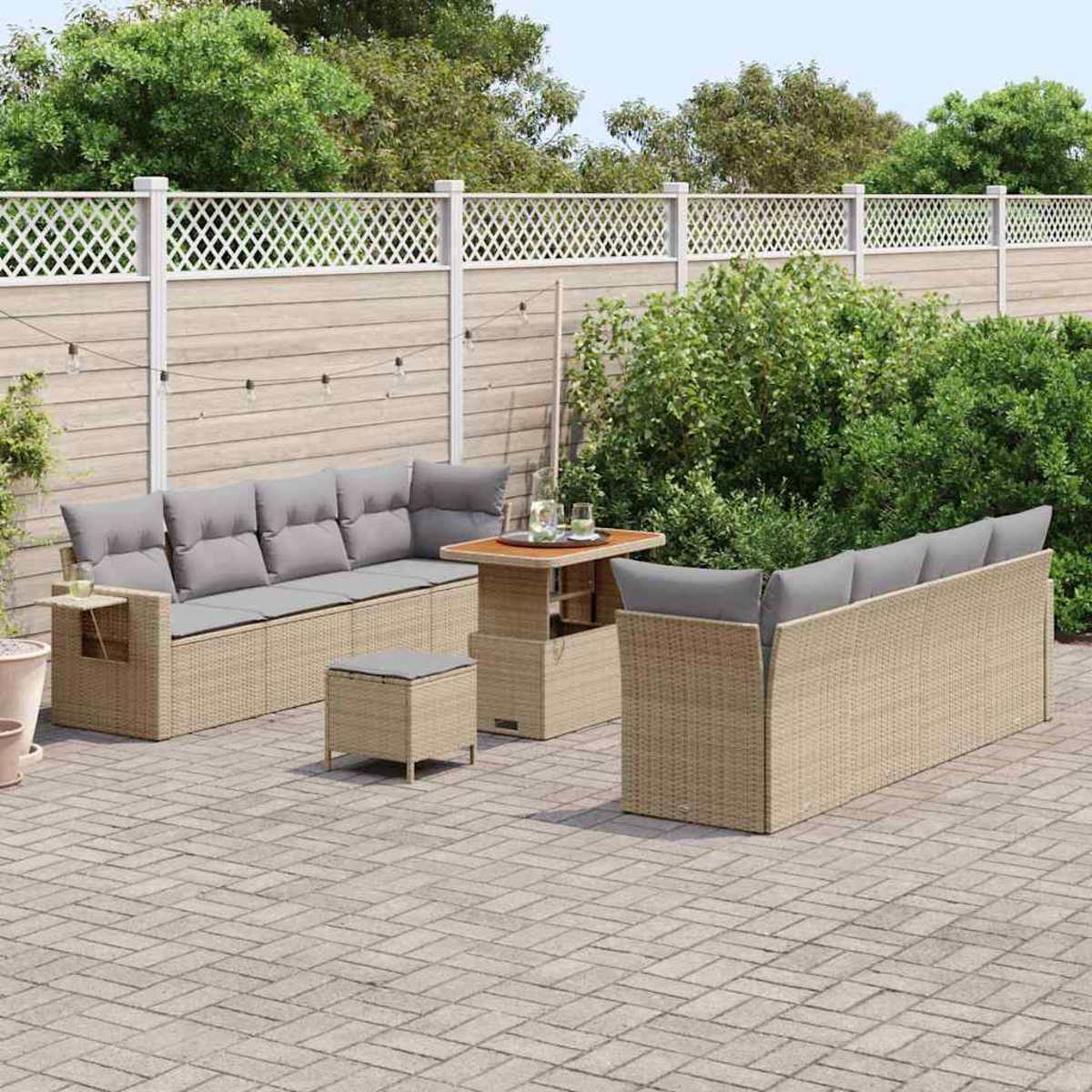 Terrassenmöbel-Set mit beigefarbenen Korbsesseln, grauen Kissen, einem Tisch und einem kleinen Hocker auf einer Ziegelterrasse, umgeben von Grün.