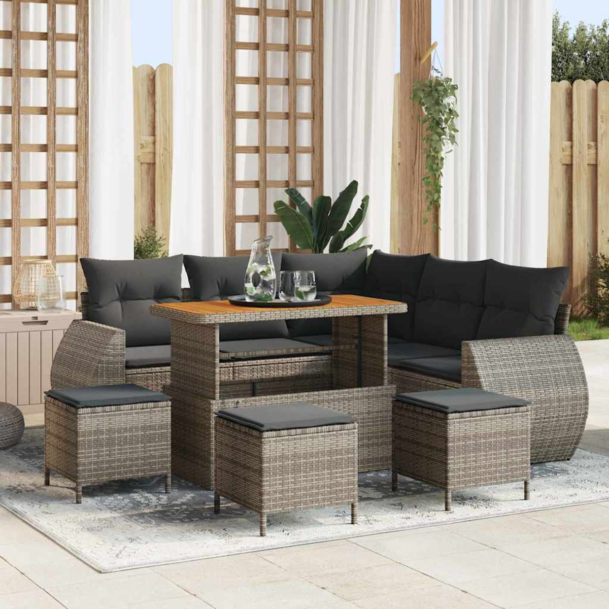 Terrassen-Set mit Korbmöbeln, schwarzen Kissen und einem Holztisch. Enthält Sofa, Hocker und einen Teppich. Vorhänge im Hintergrund.