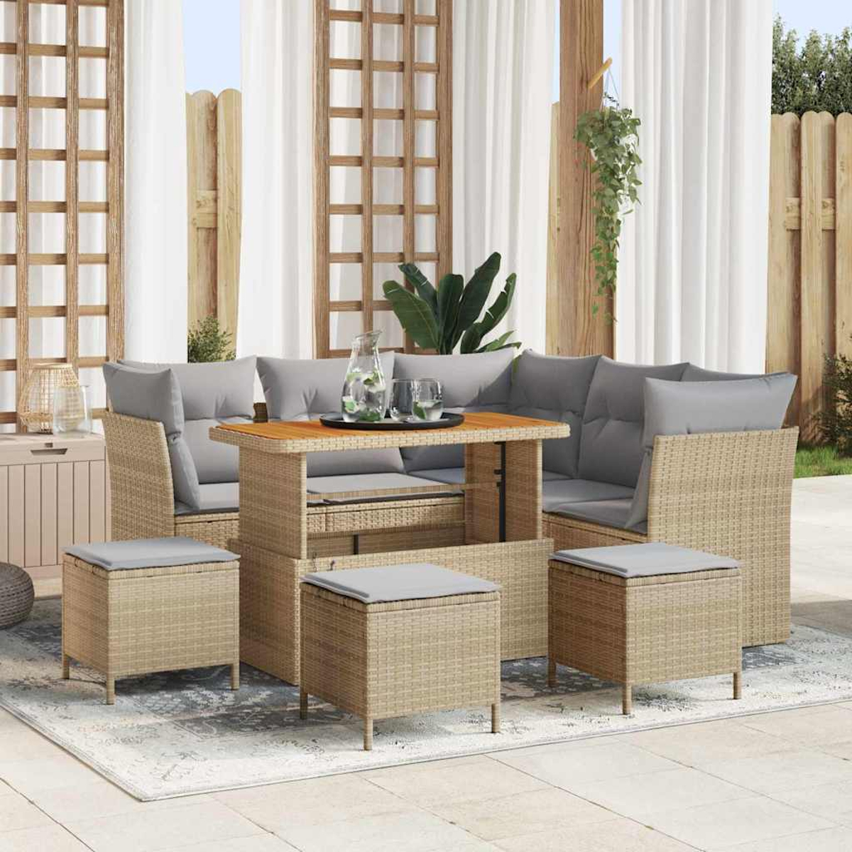 Outdoor-Korbmöbel-Set mit grauen Kissen. Tisch mit Glas und Wasser. Vorhänge und Holzzaun im Hintergrund.