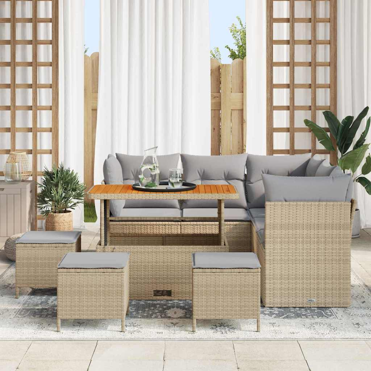Gartenmöbel-Set aus Korbgeflecht mit grauen Kissen, Tisch mit Glas und Wasser, Pflanzen und weißen Vorhängen im Hintergrund.