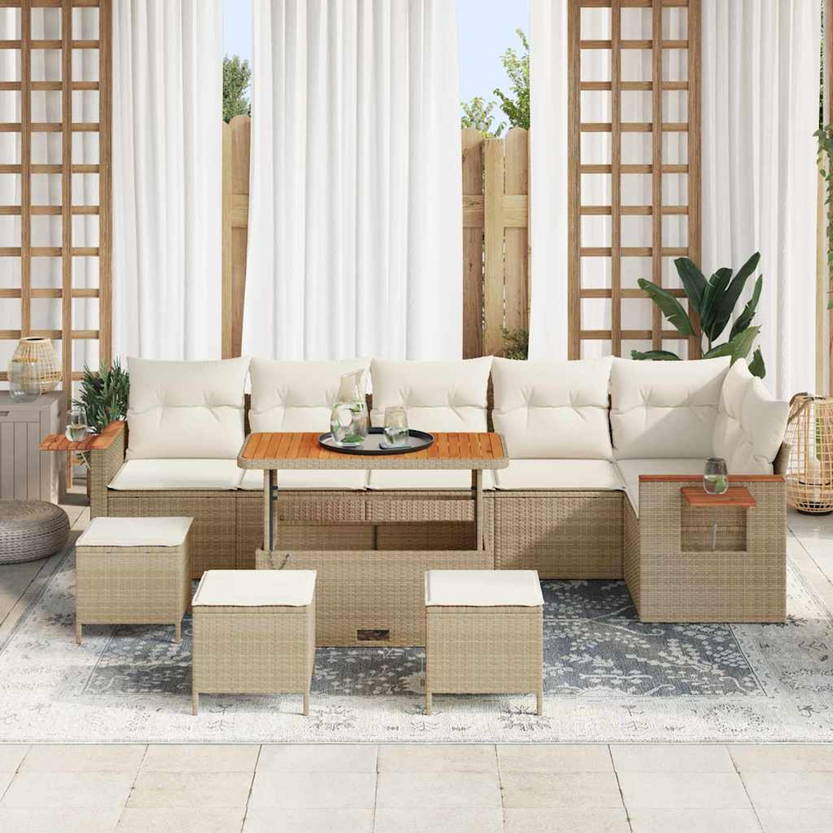 Divano angolare da esterno con cuscini color crema, tavolini e pouf. Tende bianche e una staccionata in legno sullo sfondo.