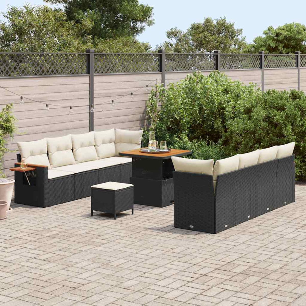 Terrassenset mit schwarzen Korbs Sofas, hellen Kissen und einem Holztisch. Inklusive kleinem Hocker, alles auf einer Ziegelsteinterrasse.