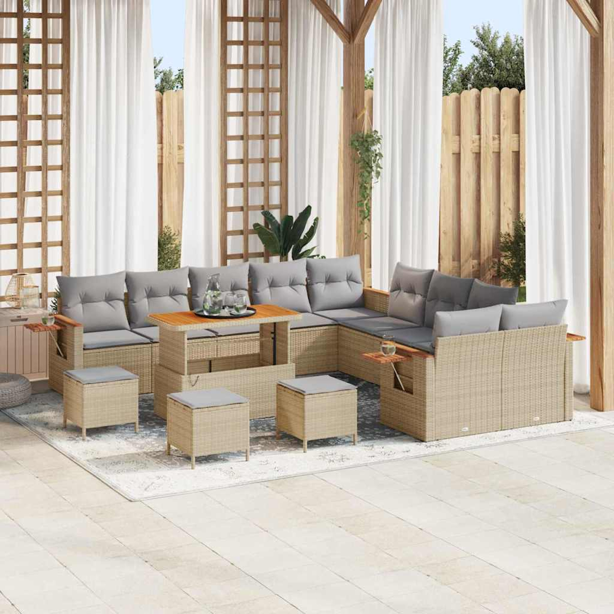 Terrassenset im Freien mit beigen Rattanmöbeln, grauen Kissen, Holztischen und einem Couchtisch. Weiße Vorhänge und ein Holzzaun im Hintergrund.