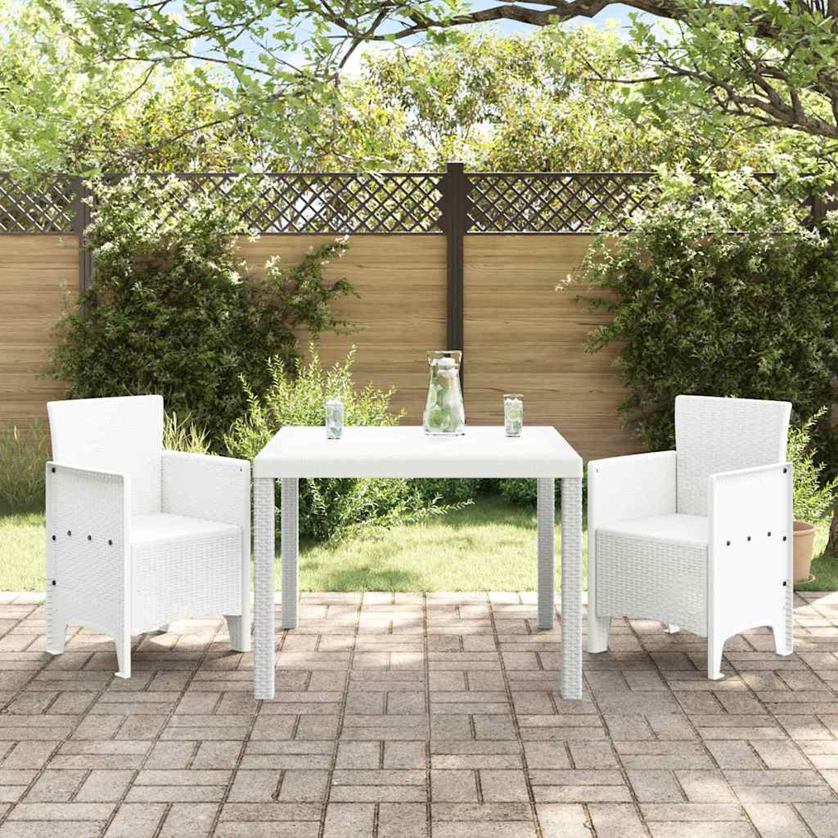 Juego de patio blanco: dos sillas y una mesa. Vasos y una jarra en la mesa. Césped verde y una valla de madera al fondo.
