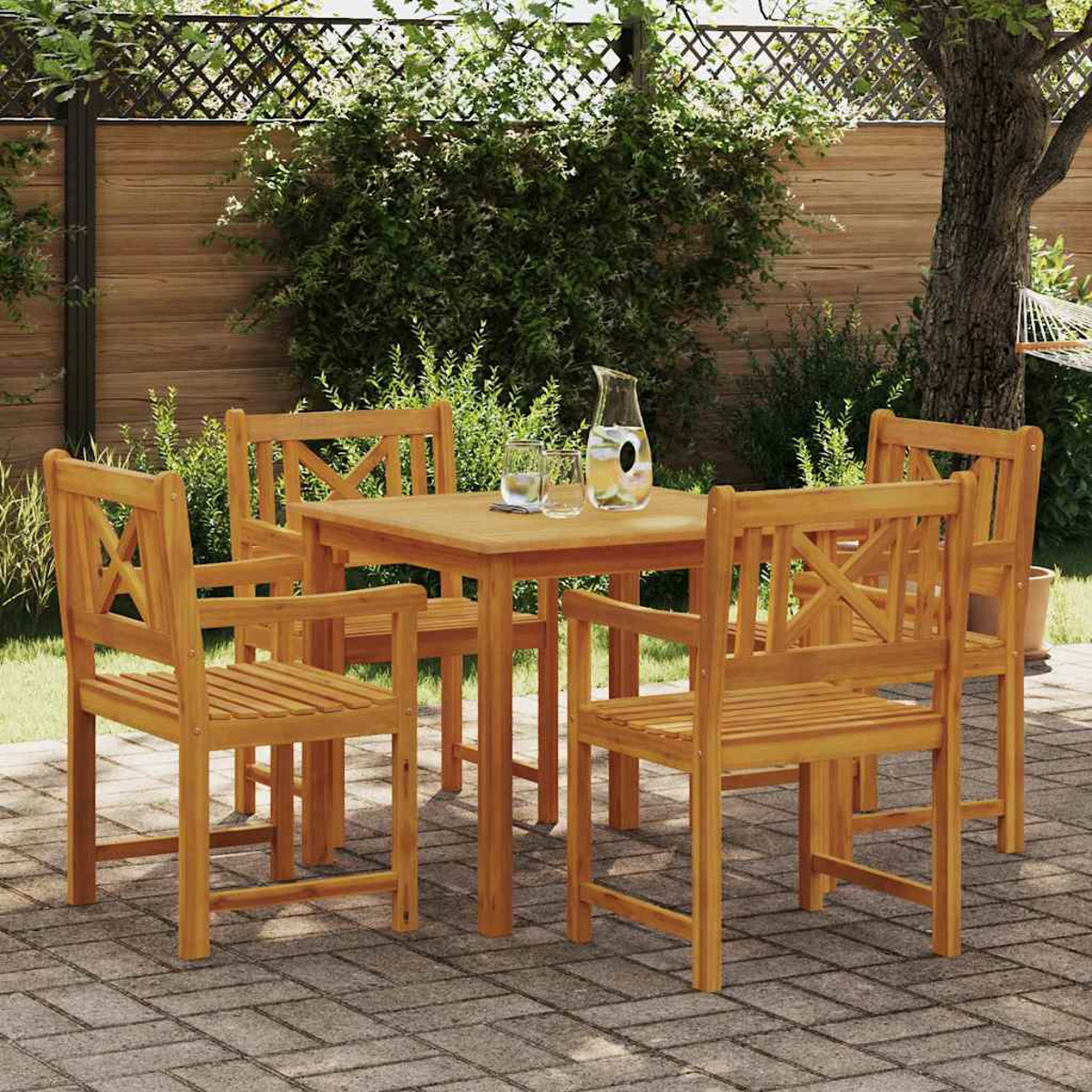 Holz-Essgarnitur für den Außenbereich mit Tisch, vier Stühlen und einer Wasserkaraffe. Auf einer Ziegelterrasse mit Grün im Hintergrund.