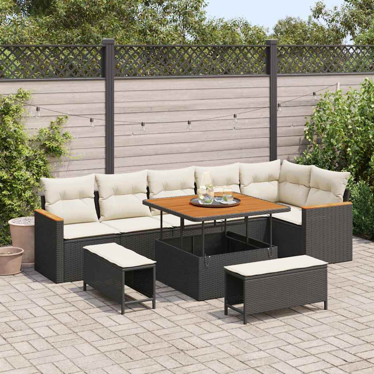 Gartenmöbel-Set. Ecksofa mit cremefarbenen Kissen, Couchtisch und zwei Ottomanen auf gepflasterter Terrasse.