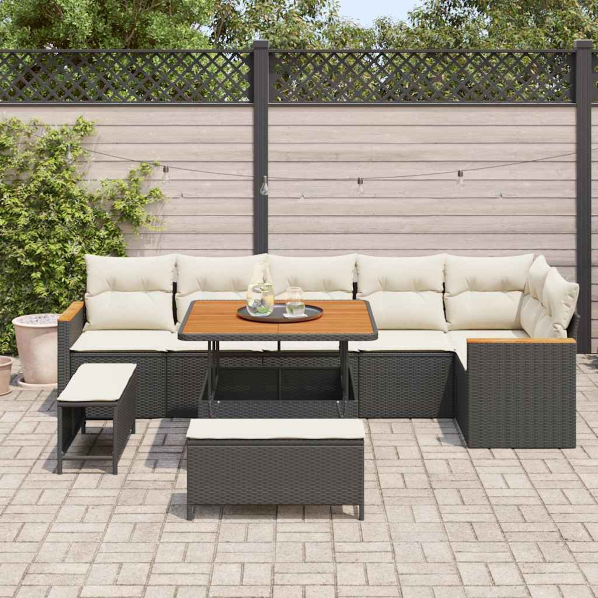 Garten-Sitzgruppe mit cremefarbenen Kissen, Holztisch und zwei Bänken. Ein Holzzaun und Blätterwerk sind im Hintergrund.