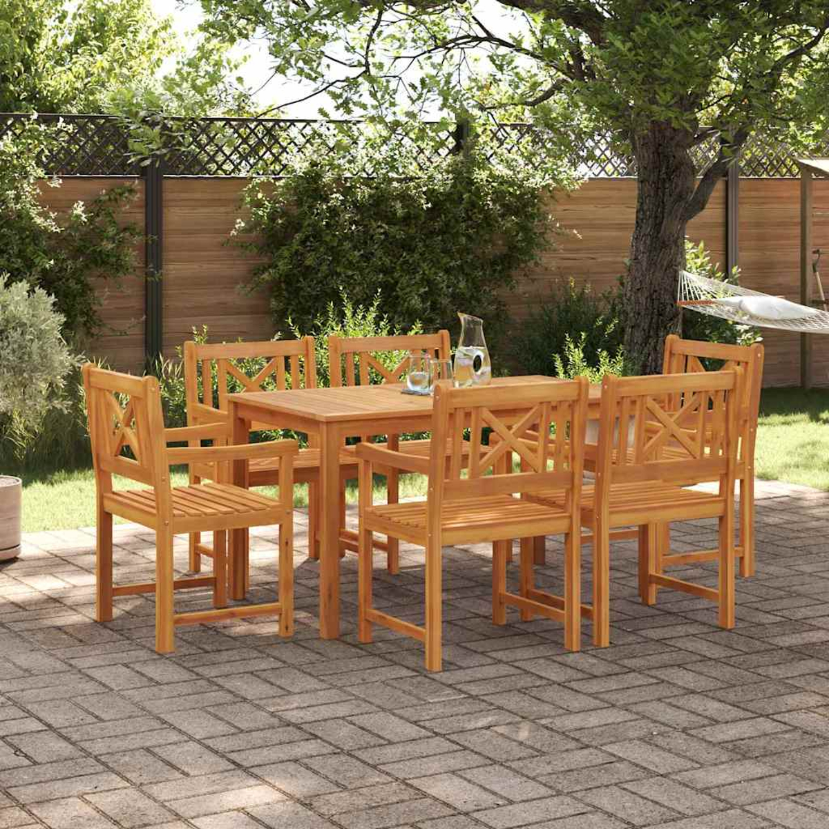 Juego de comedor de madera al aire libre con mesa, sillas y una jarra en un patio de ladrillos. Una hamaca cuelga al fondo.