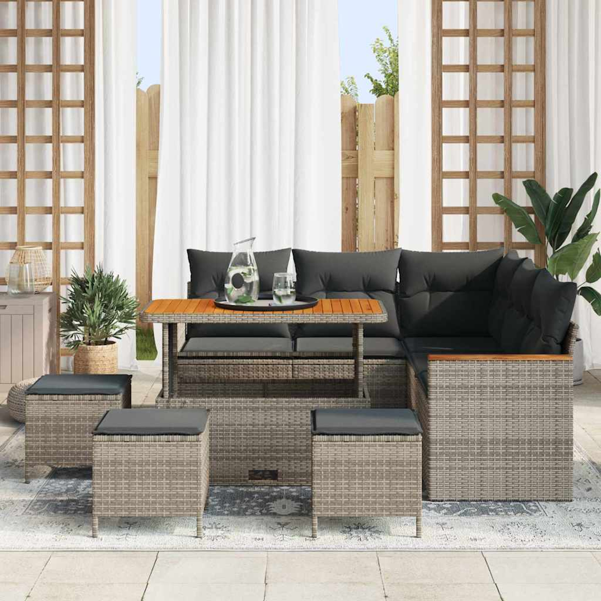 Garten-Terrassenset. Graues Korbmöbel-Sofa, Tisch und Hocker mit dunklen Kissen. Pflanzen, weiße Vorhänge und Holzgitter im Hintergrund.