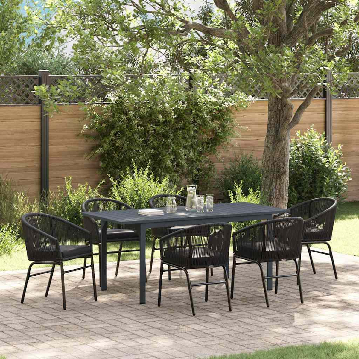 Ein dunkelgrauer Tisch und sechs Stühle auf einer Terrasse. Ein Baum und ein Holzzaun sind im Hintergrund. Gläser und ein Krug stehen auf dem Tisch.