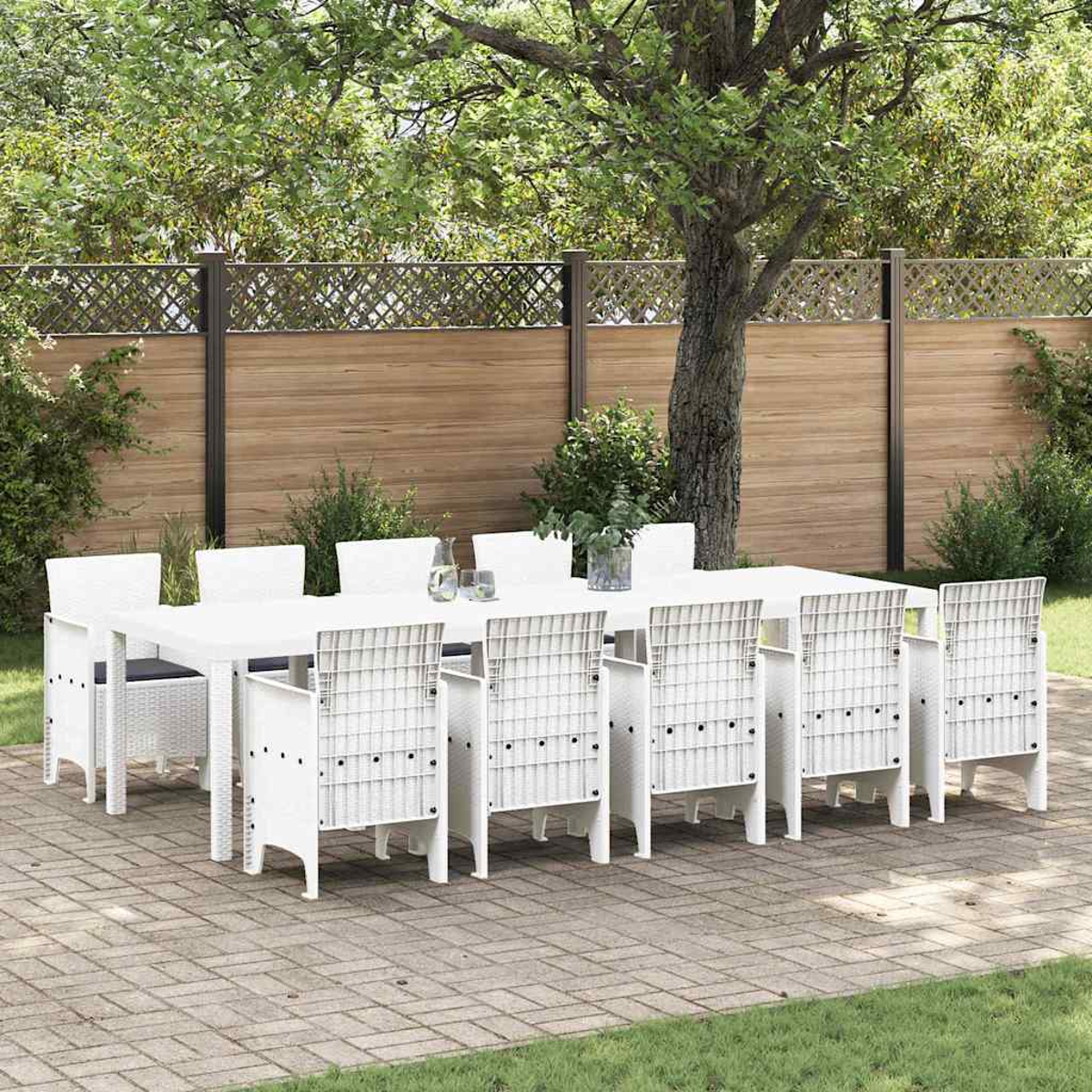 Essgruppe im Freien mit weißem Tisch und Stühlen auf einer Ziegelterrasse. Im Hintergrund ein Holzzaun und ein Baum.