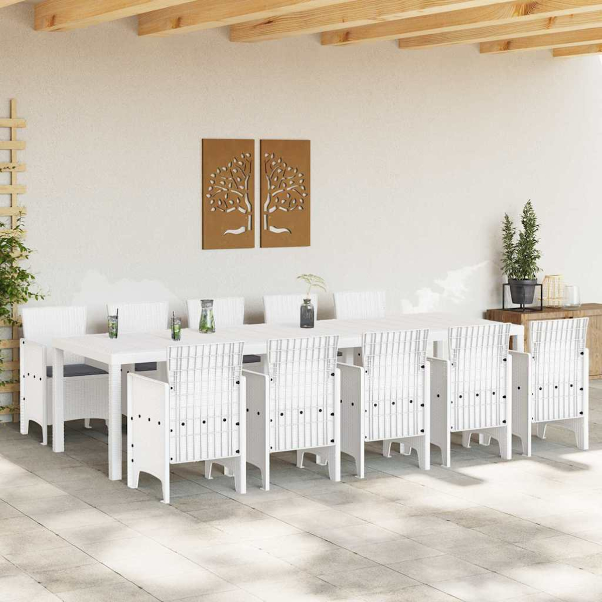 Essgruppe im Freien mit weißen Stühlen und Tisch. Zwei Baumkunstwerke an der Wand. Pflanzen und Holzbalken darüber.