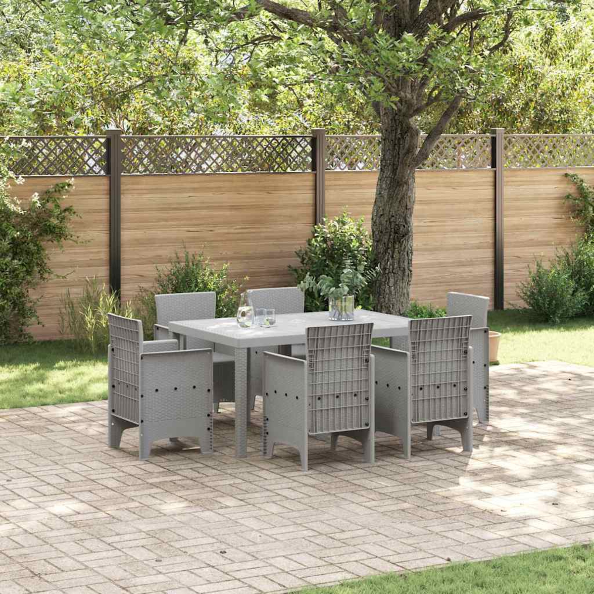 Ein graues Terrassenset mit sechs Stühlen und einem Tisch steht auf einer Ziegelterrasse. Im Hintergrund sind ein Holzzaun und grüne Bäume zu sehen.