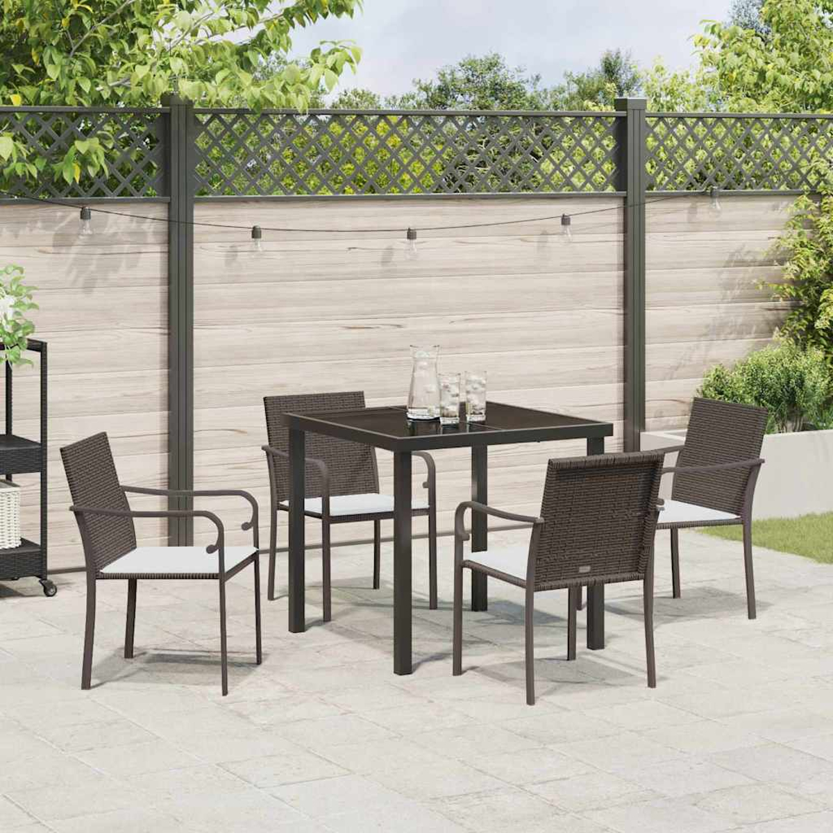 Terrassenset im Freien. Quadratischer dunkler Tisch mit vier Stühlen. Weiße Kissen. Holzzaun Hintergrund, Lichterketten, Grün.