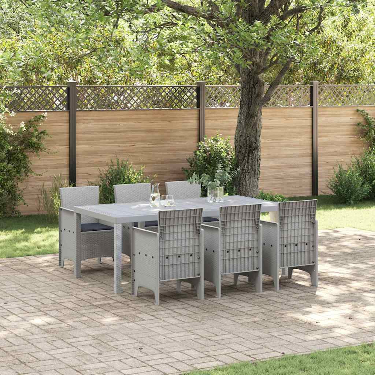 Ein grauer Tisch mit sechs Stühlen steht auf einer Ziegelterrasse. Ein Holzzaun und Bäume bilden den Hintergrund, wodurch eine Gartenszene entsteht.