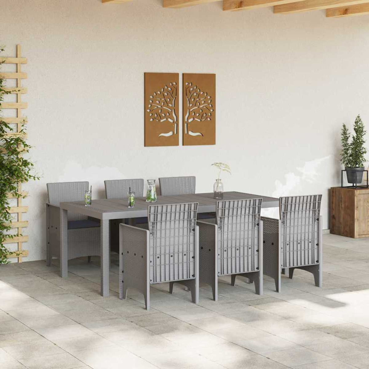 Essgruppe im Freien. Grauer Tisch und Stühle auf der Terrasse. Zwei Baumkunstwerke an der Wand. Pflanzen im Hintergrund.