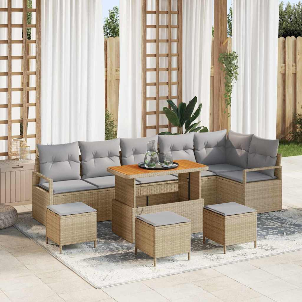 Outdoor-Sitzgruppe mit grauen Kissen, Couchtisch und Hockern. Weiße Vorhänge und Holzgitter im Hintergrund.