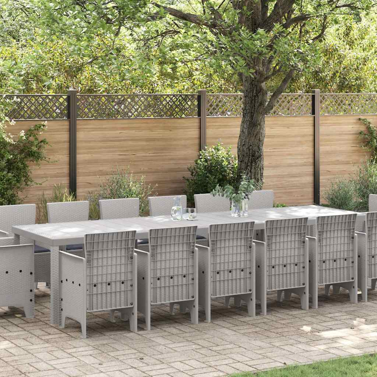 Essgruppe im Freien: ein langer Tisch und Stühle. Ein Holzzaun und Bäume im Hintergrund. Die Szene spielt auf einer Terrasse.