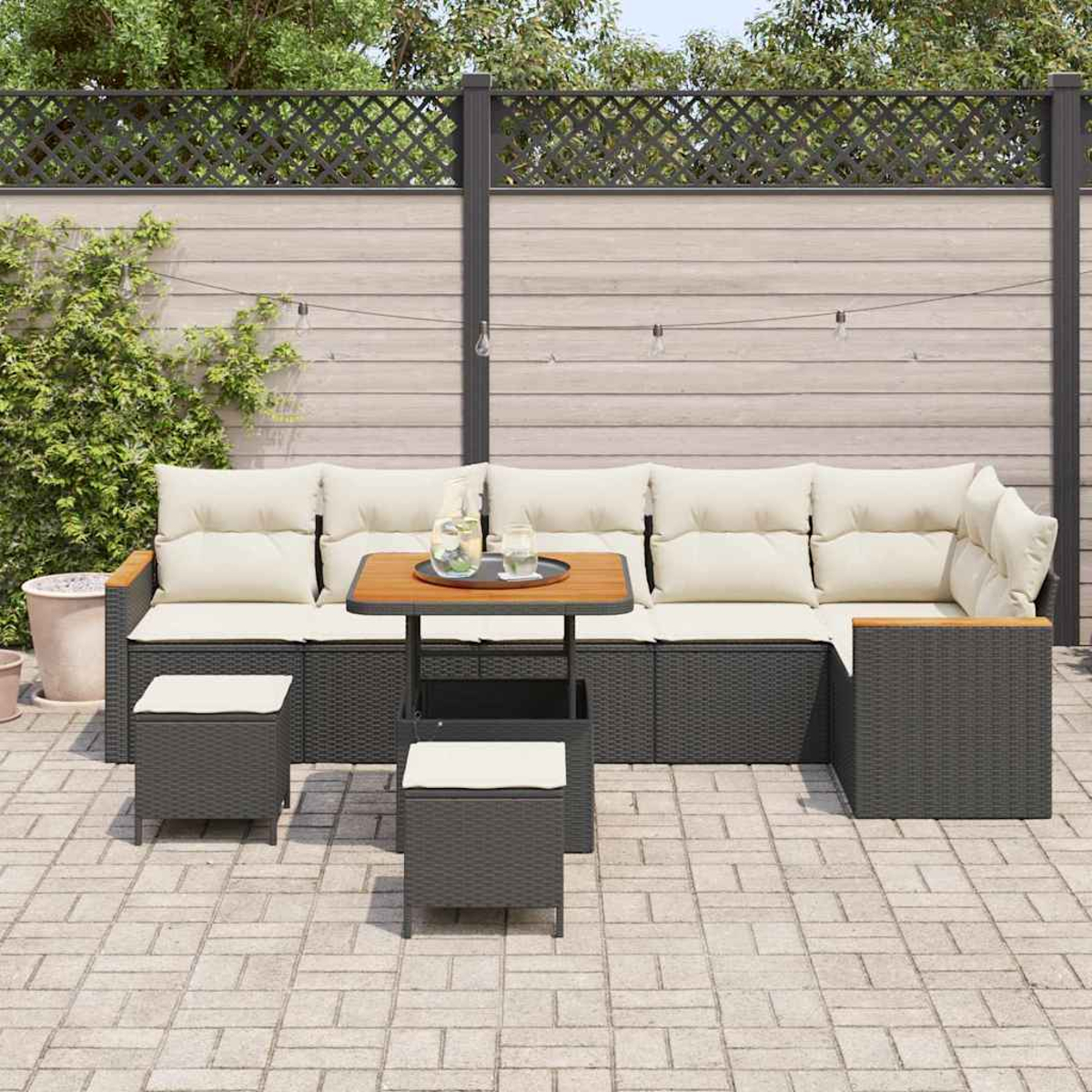 Garten-Set mit dunkelgrauen Korbmöbeln, cremefarbenen Kissen und einem Holztisch. Ein Zaun und Grün im Hintergrund.