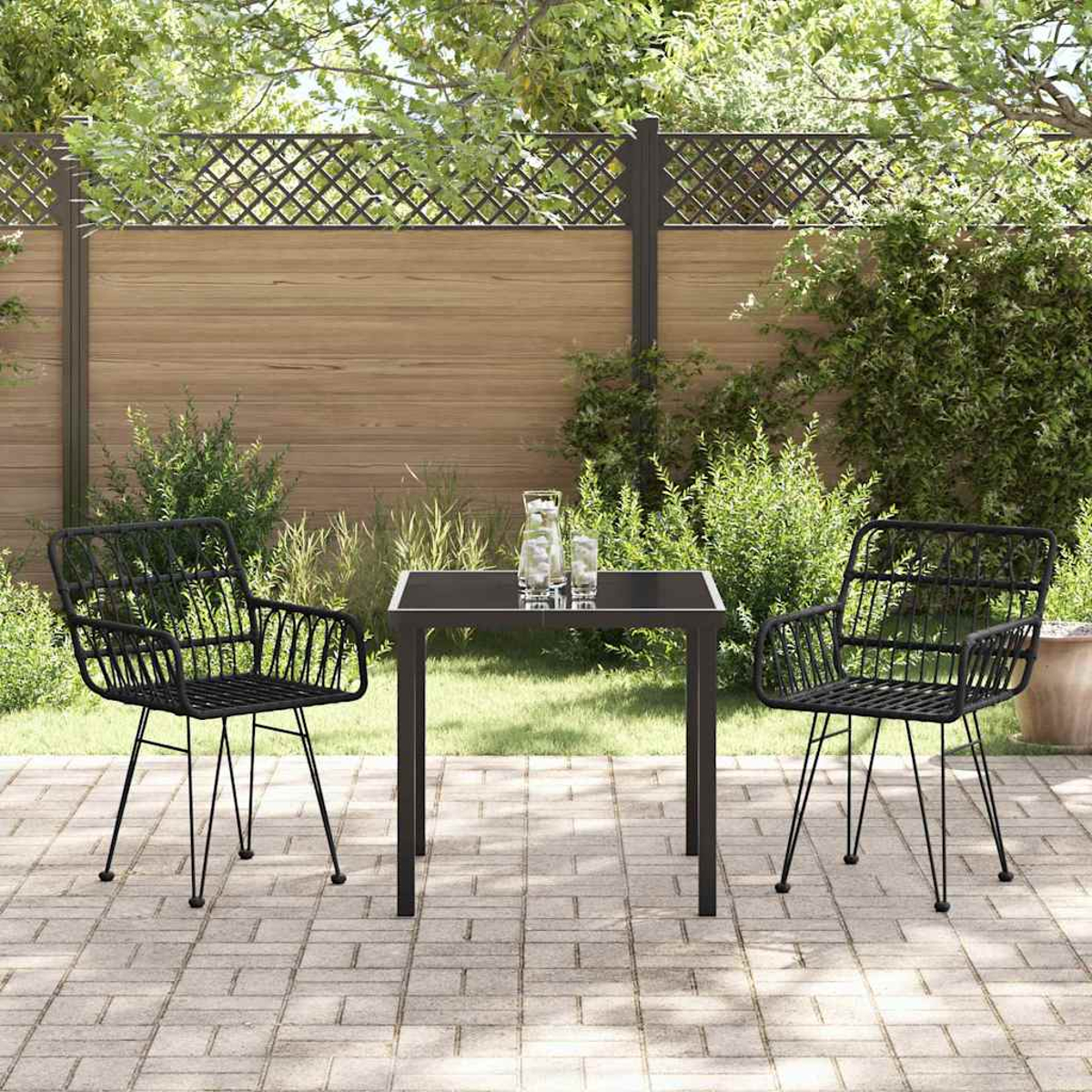 Szene im Freien mit schwarzem Tisch und Stühlen auf einer Terrasse. Hoher Holzzaun mit Gitterdetail, grüne Büsche und Gras.