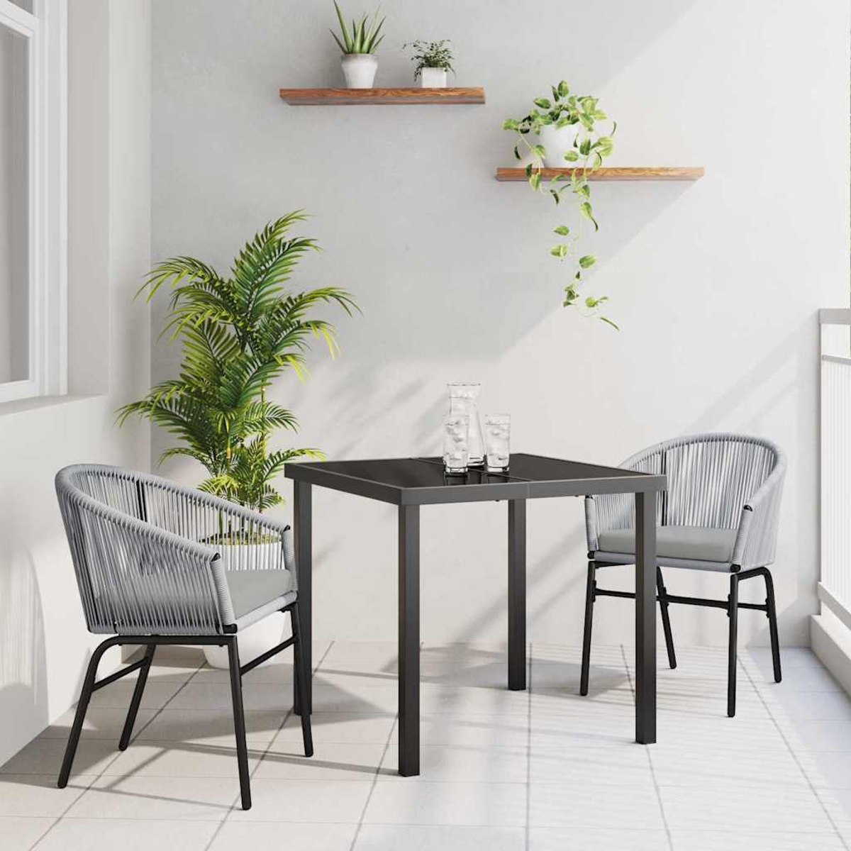 Eine Terrasse mit einem quadratischen Tisch, zwei Stühlen, Pflanzen und Regalen. Auf dem Tisch stehen Gläser. Weiße Wände und Boden.