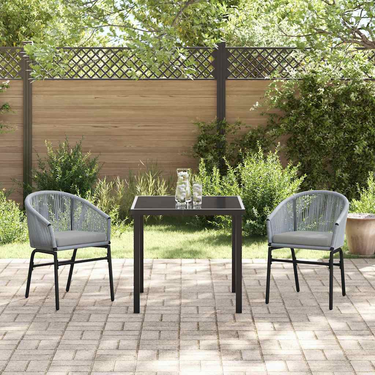 Terrassenset im Freien mit zwei grauen Stühlen, einem schwarzen Tisch und einem Holzzaun. Gläser und eine Karaffe stehen auf dem Tisch.