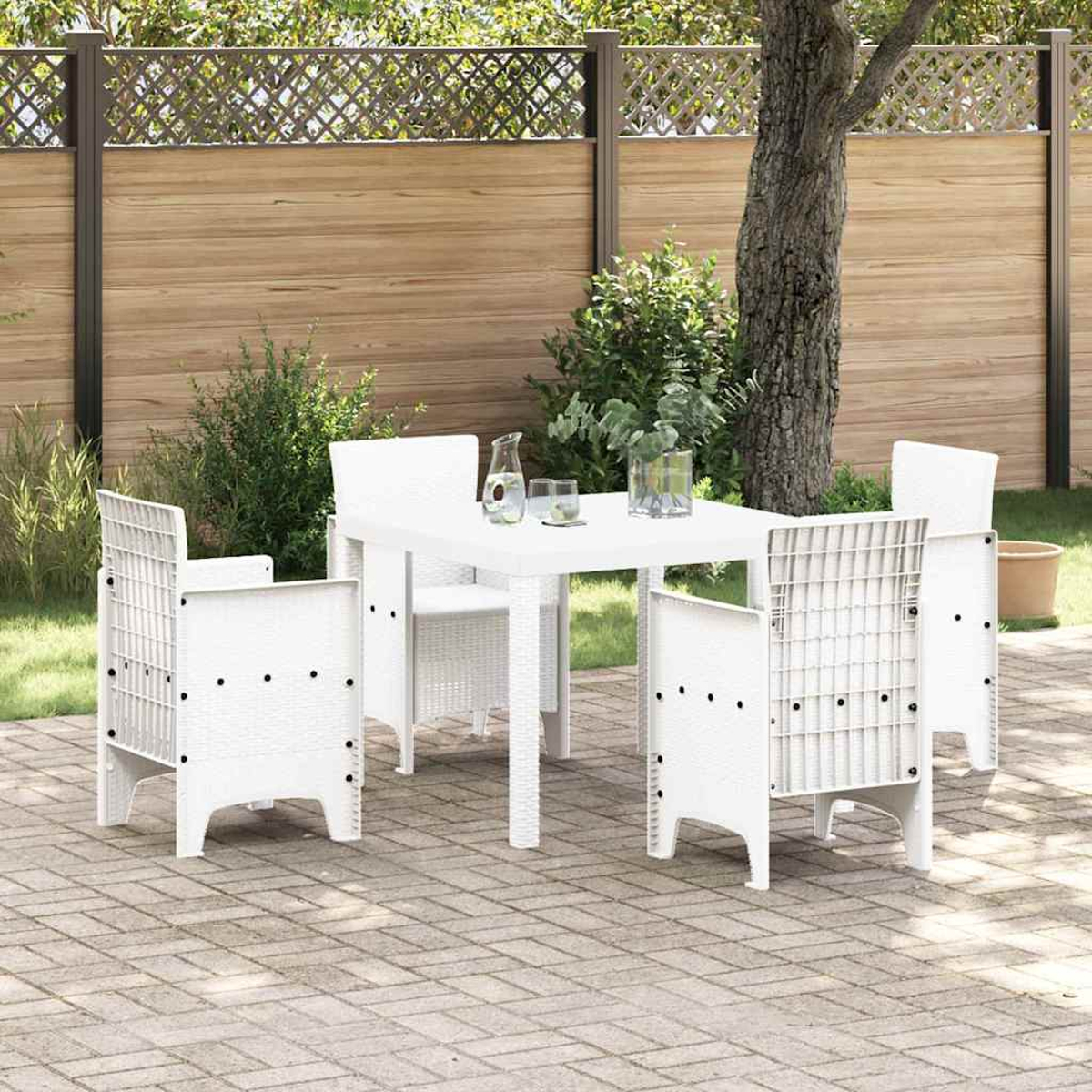 Ein weißer Tisch und Stühle stehen auf einer Terrasse. Im Hintergrund befinden sich ein Zaun und ein Baum. Auf dem Tisch stehen eine Wasserkaraffe und Gläser.