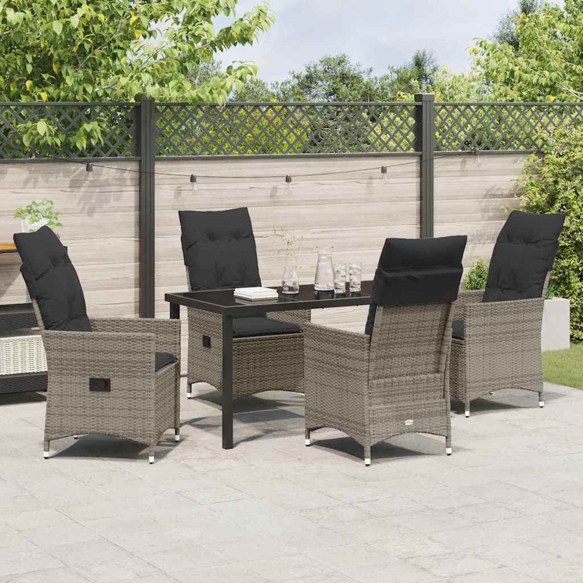 Eine Terrasse zeigt einen Tisch und vier Stühle. Jeder Stuhl hat ein schwarzes Kissen. Hintergrund ist ein Zaun und grüne Pflanzen.