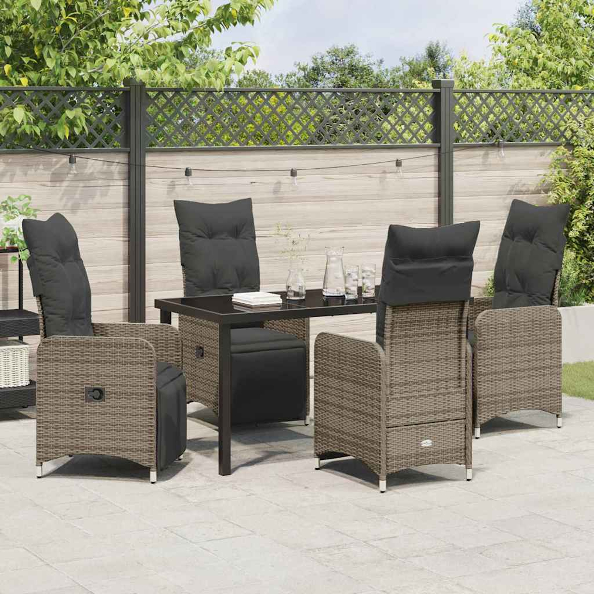 Terrassenset mit schwarzem Tisch, grauen Stühlen mit schwarzen Kissen und einem dekorativen Zaun im Hintergrund. Klarer Tag.