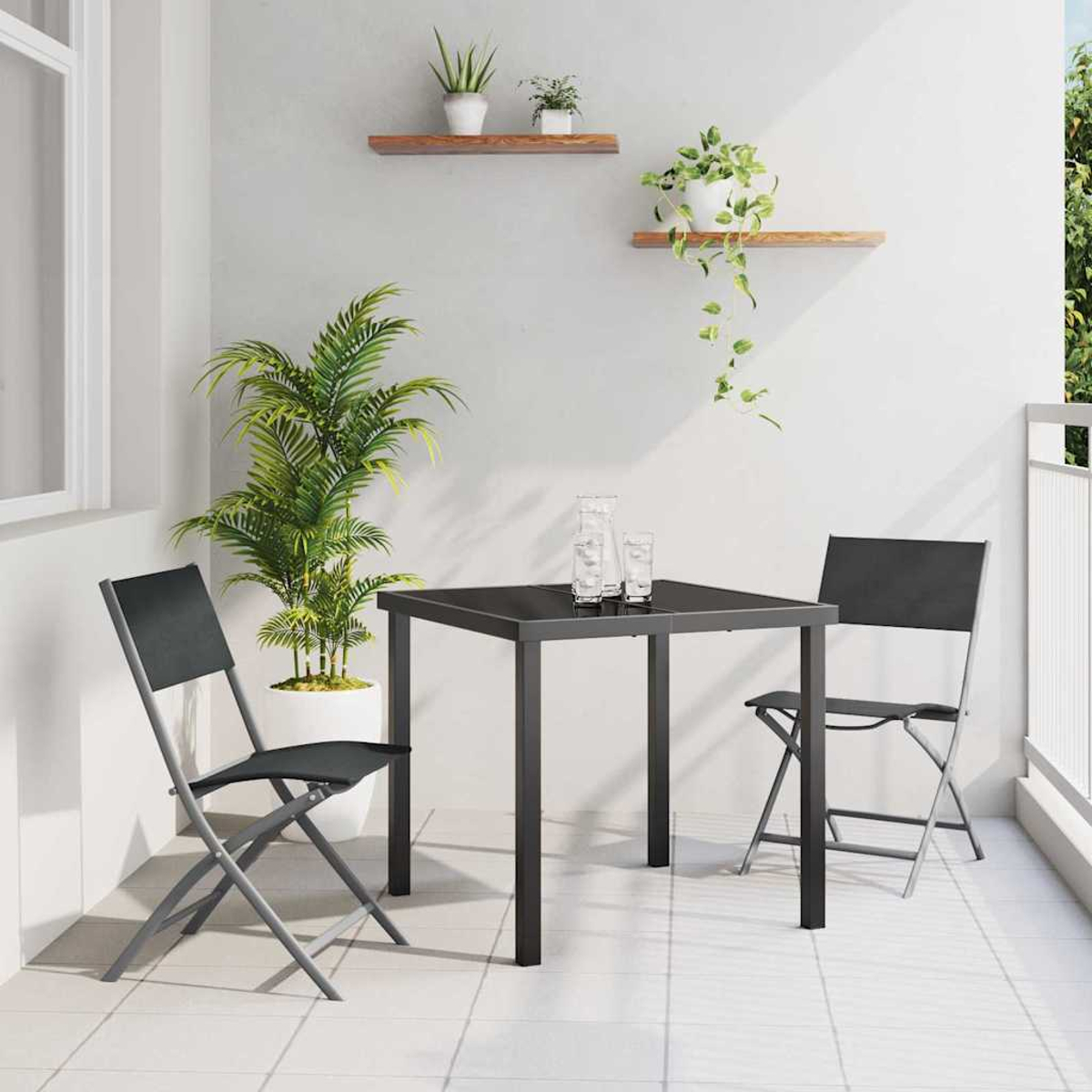 Ein kleiner Balkon mit Tisch, zwei Stühlen und Pflanzen. Zwei Gläser auf dem Tisch. Weiße Wände und Bodenfliesen.