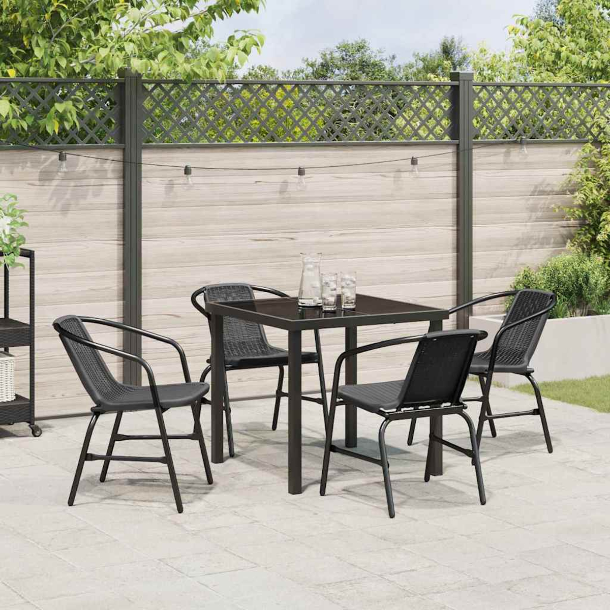 Terrassenset im Freien. Schwarzer quadratischer Tisch mit vier passenden Stühlen. Klare Gläser und Krug auf dem Tisch. Holzzaun im Hintergrund.