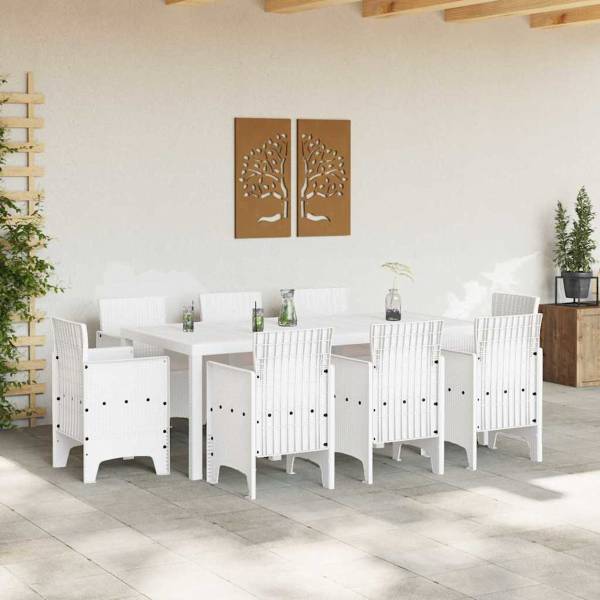 Essgruppe im Freien mit weißem Tisch und Stühlen. Dekorative Baumtafeln hängen an der weißen Wand. Pflanzen in Töpfen sind ebenfalls sichtbar.