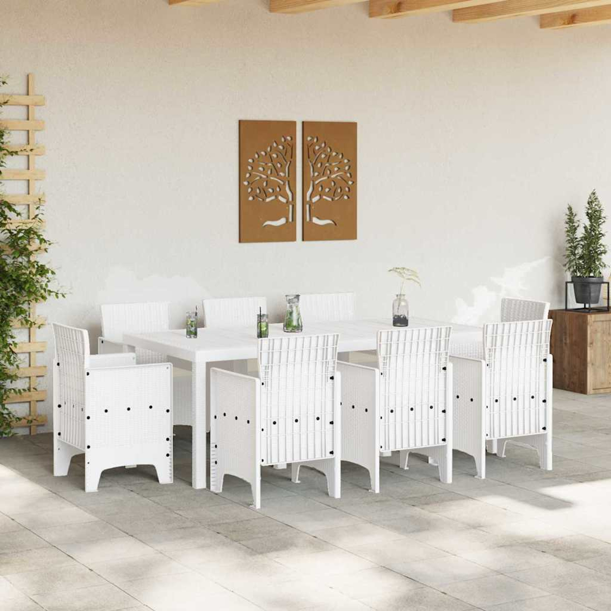 Essgruppe im Freien mit weißen Stühlen und Tisch. Braune Baumkunst an der Wand. Pflanzen und Holzkiste im Hintergrund.