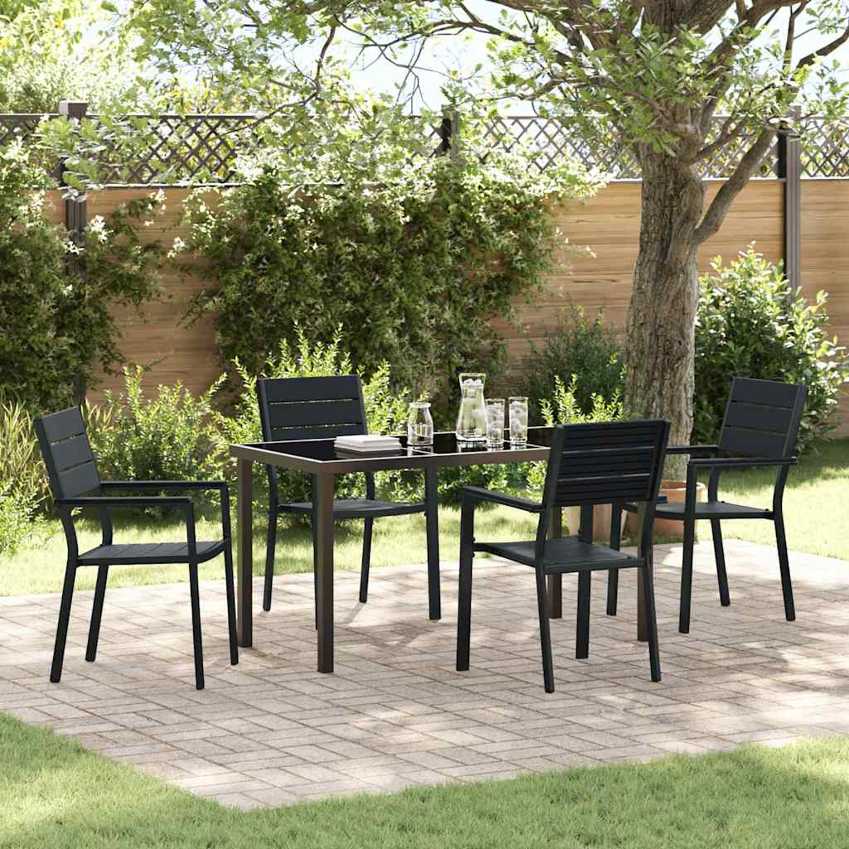 Essgruppe im Freien: ein schwarzer Tisch mit vier passenden Stühlen, Gläsern und einer Kanne auf einer Ziegelterrasse, mit einem Baum im Hintergrund.