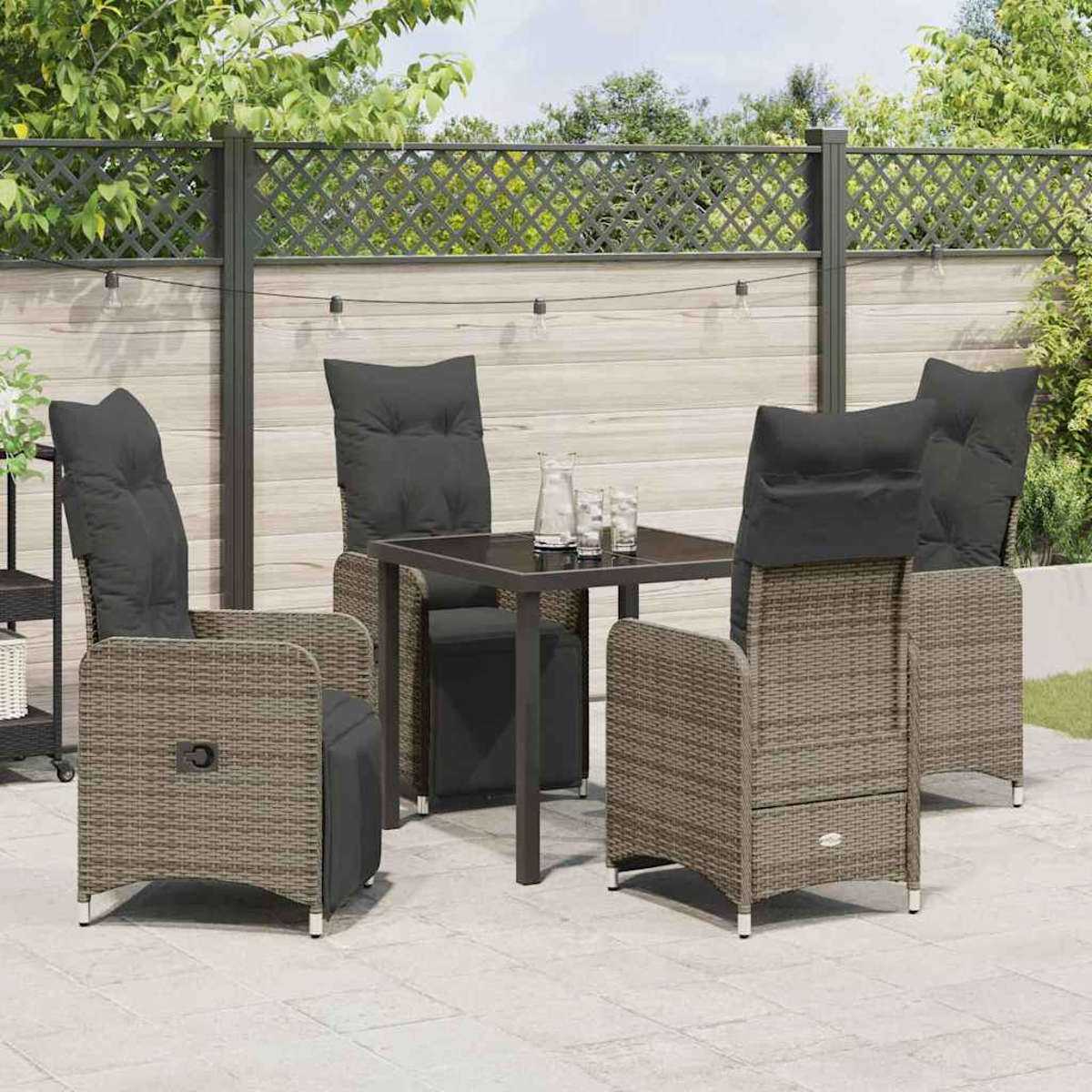 Terrassenset mit vier Korbstühlen mit schwarzen Kissen um einen quadratischen Tisch. Hintergrund: Zaun und Grün.