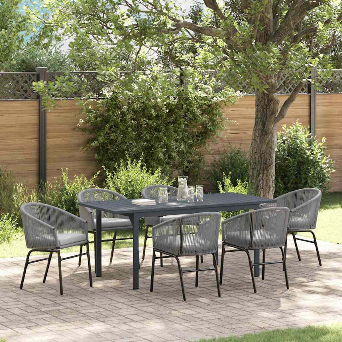 Essgarnitur im Freien. Grauer Tisch und Stühle auf einer Terrasse. Ein Baum und ein Zaun sind im Hintergrund. Krug und Gläser auf dem Tisch.