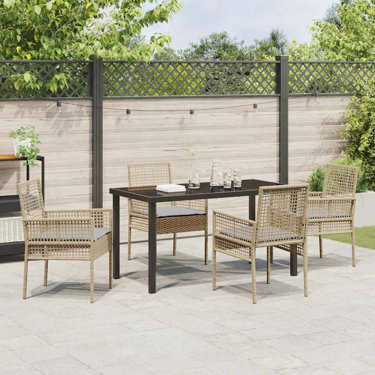 Set da patio esterno con tavolo e sedie. Una staccionata in legno sullo sfondo. Le sedie hanno un intreccio marrone chiaro e cuscini grigi.