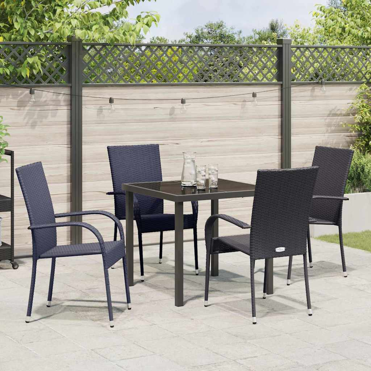 Terrassenmöbel mit vier Stühlen, einem quadratischen Tisch und einem dekorativen Zaun im Hintergrund. Gläser und eine Wasserkaraffe stehen auf dem Tisch.