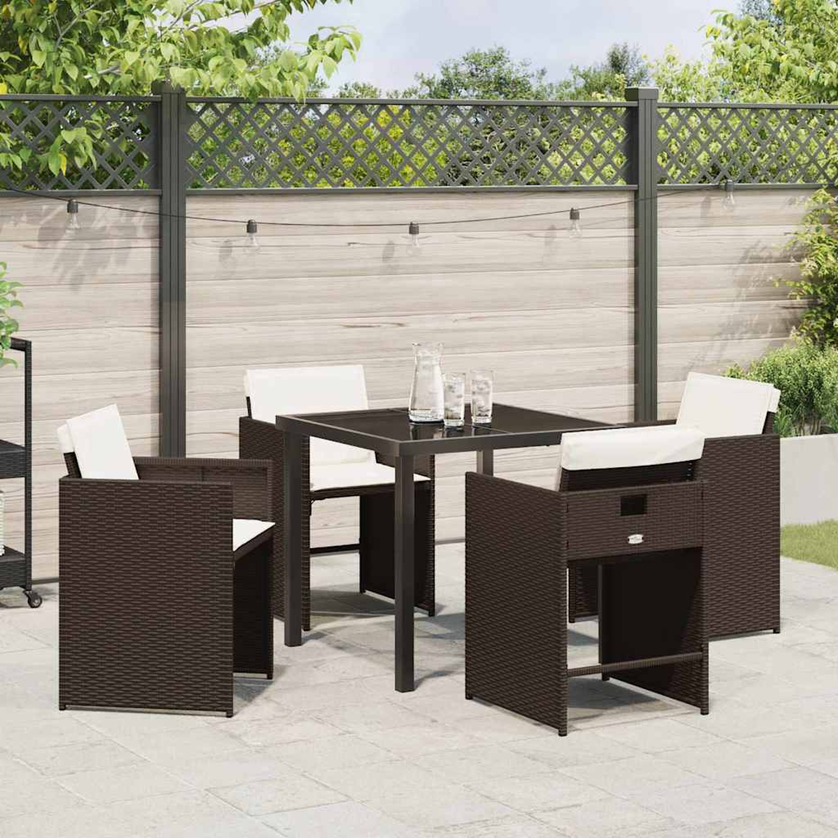 Terrassen-Set mit braunen Korbstühlen und einem Tisch mit Gläsern und einem Wasserkrug. Im Hintergrund ist ein Zaun.
